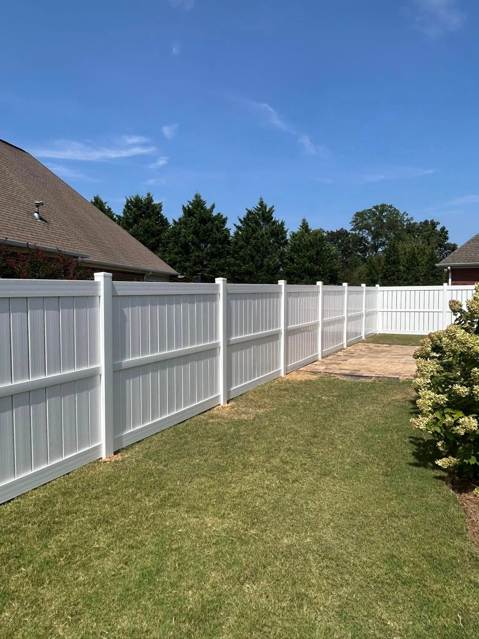 White vinyl fence in a grassy backyard, blue sky overhead.