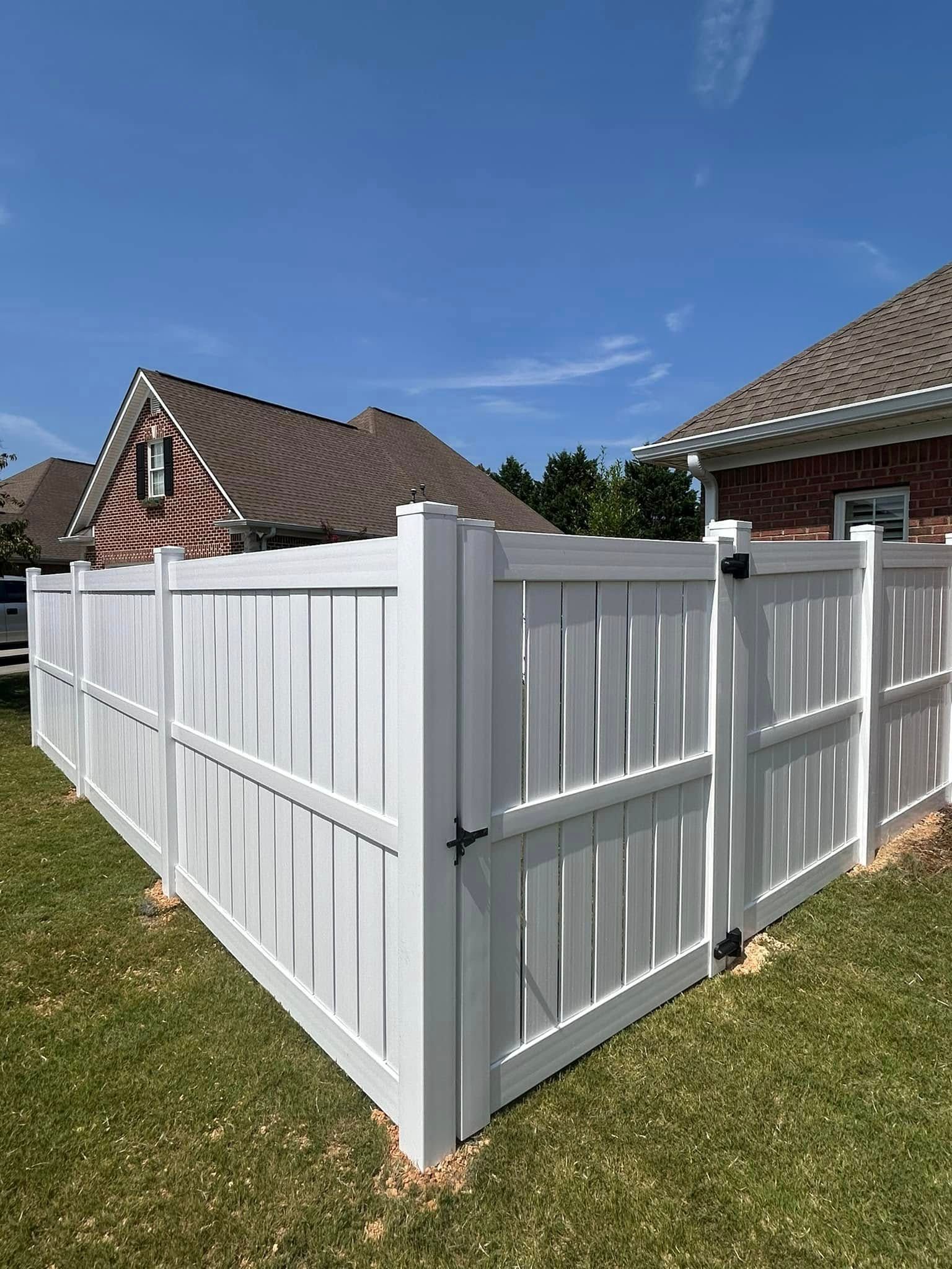 White vinyl fence enclosing a backyard with gate, under a clear blue sky.