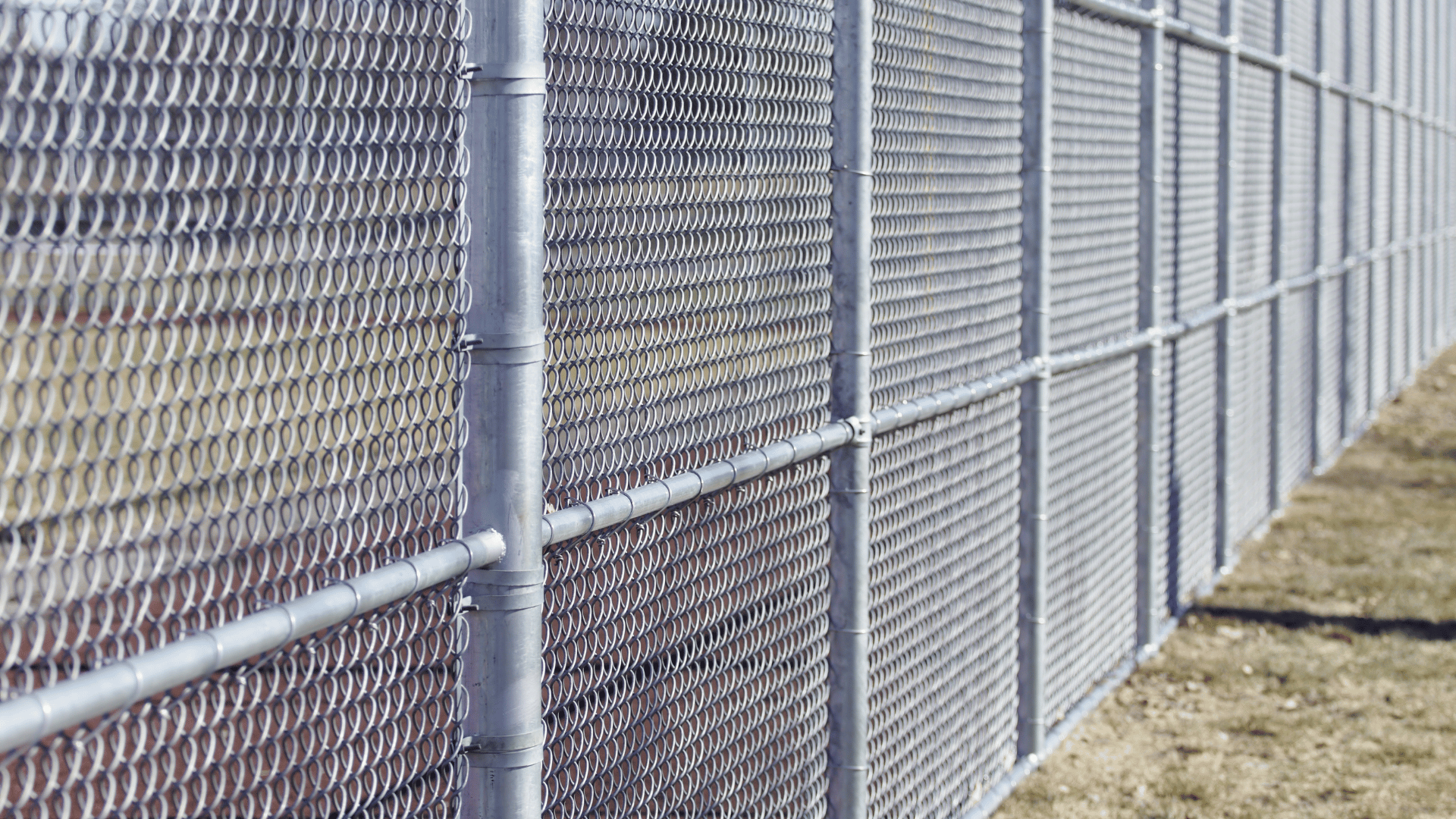 Metal fence, gray posts and horizontal supports, expanded metal mesh, outdoors.