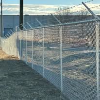 Chain-link fence with barbed wire on top, outside a building under a blue sky.