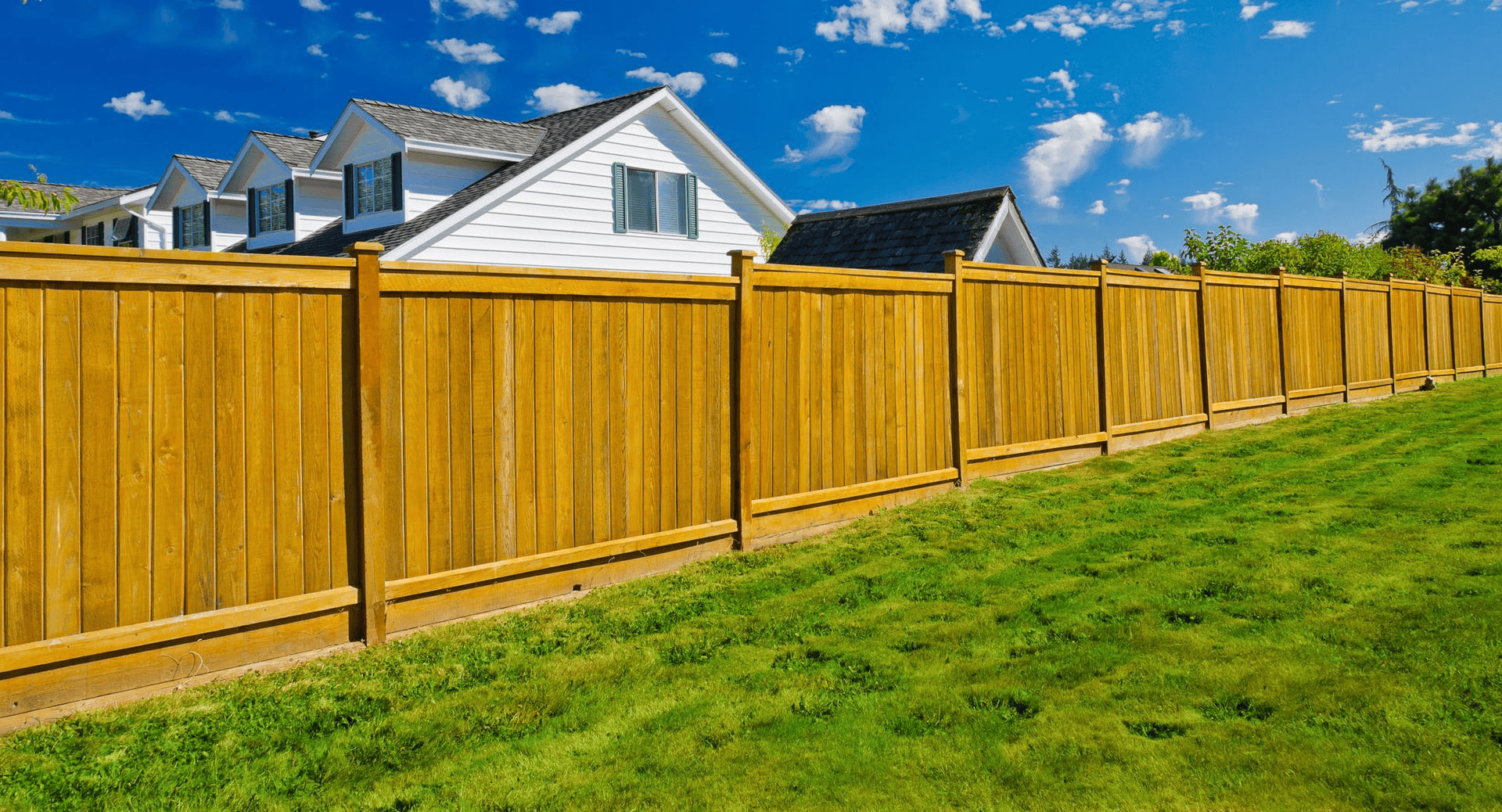 Wooden fence surrounds a house with a green lawn under a blue sky.