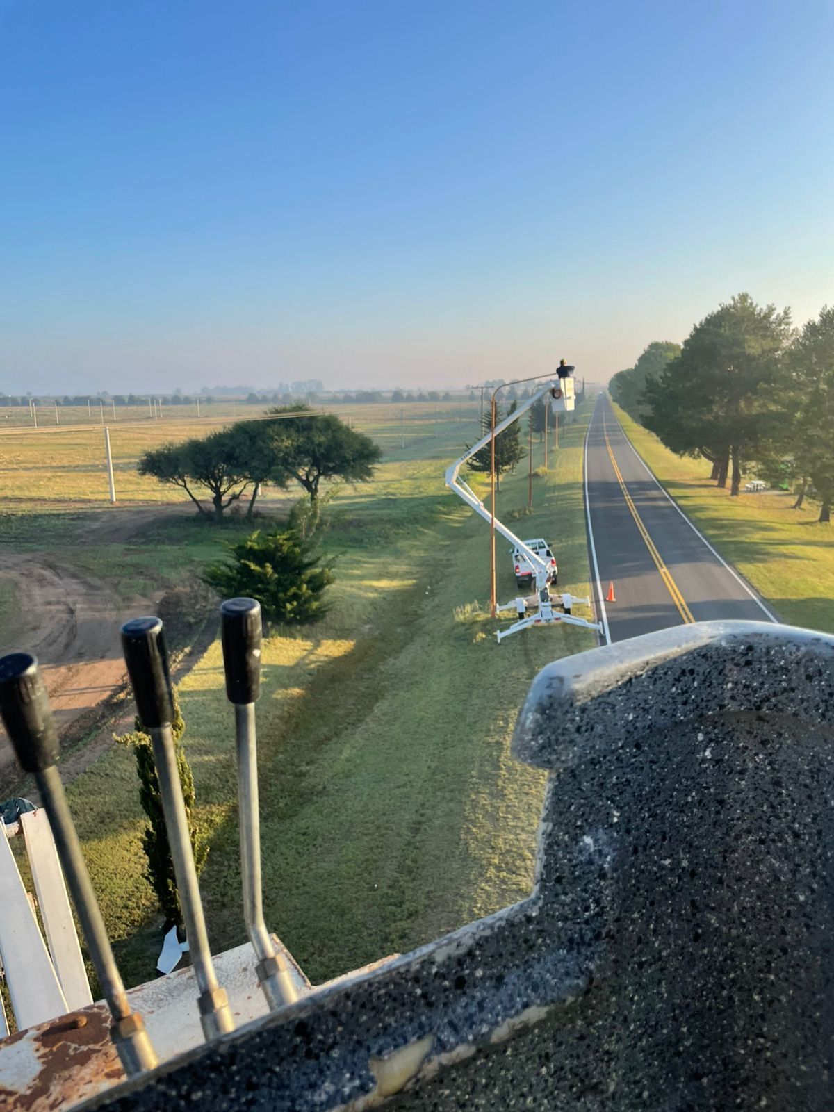 Una carretera se extiende a lo lejos, con un camión utilitario y controles en primer plano. Campos y árboles 