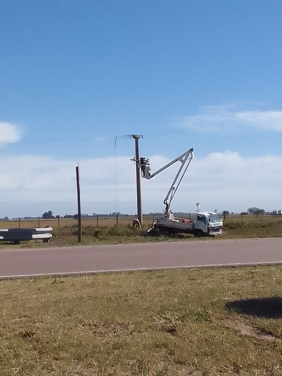 Camión utilitario con plataforma elevada trabajando en un poste de línea eléctrica en un día soleado.