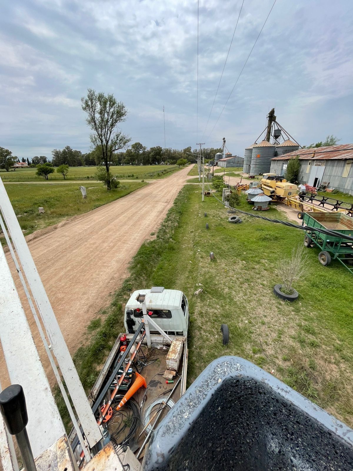 Vista de camión de un camino rural, césped verde y edificios agrícolas bajo un cielo nublado.
