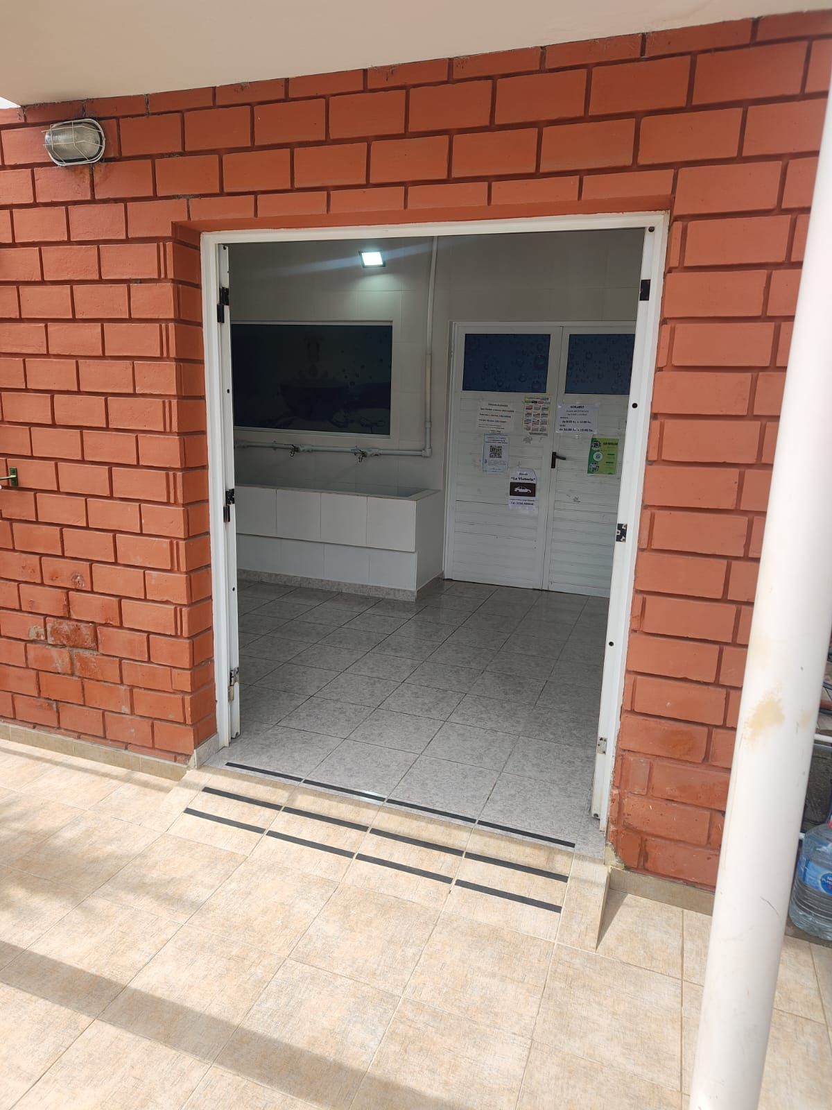 Entrada a edificio de ladrillo con puerta abierta, interior visible: suelo de baldosas