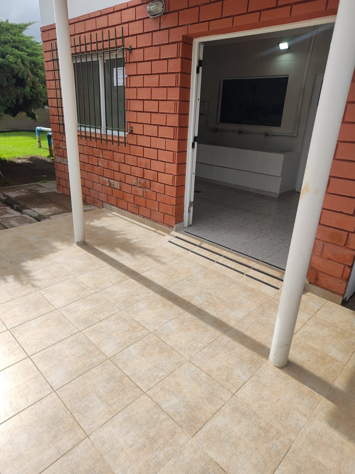 Patio con suelo de baldosas y edificio de ladrillo con puerta abierta, mostrando el interior.