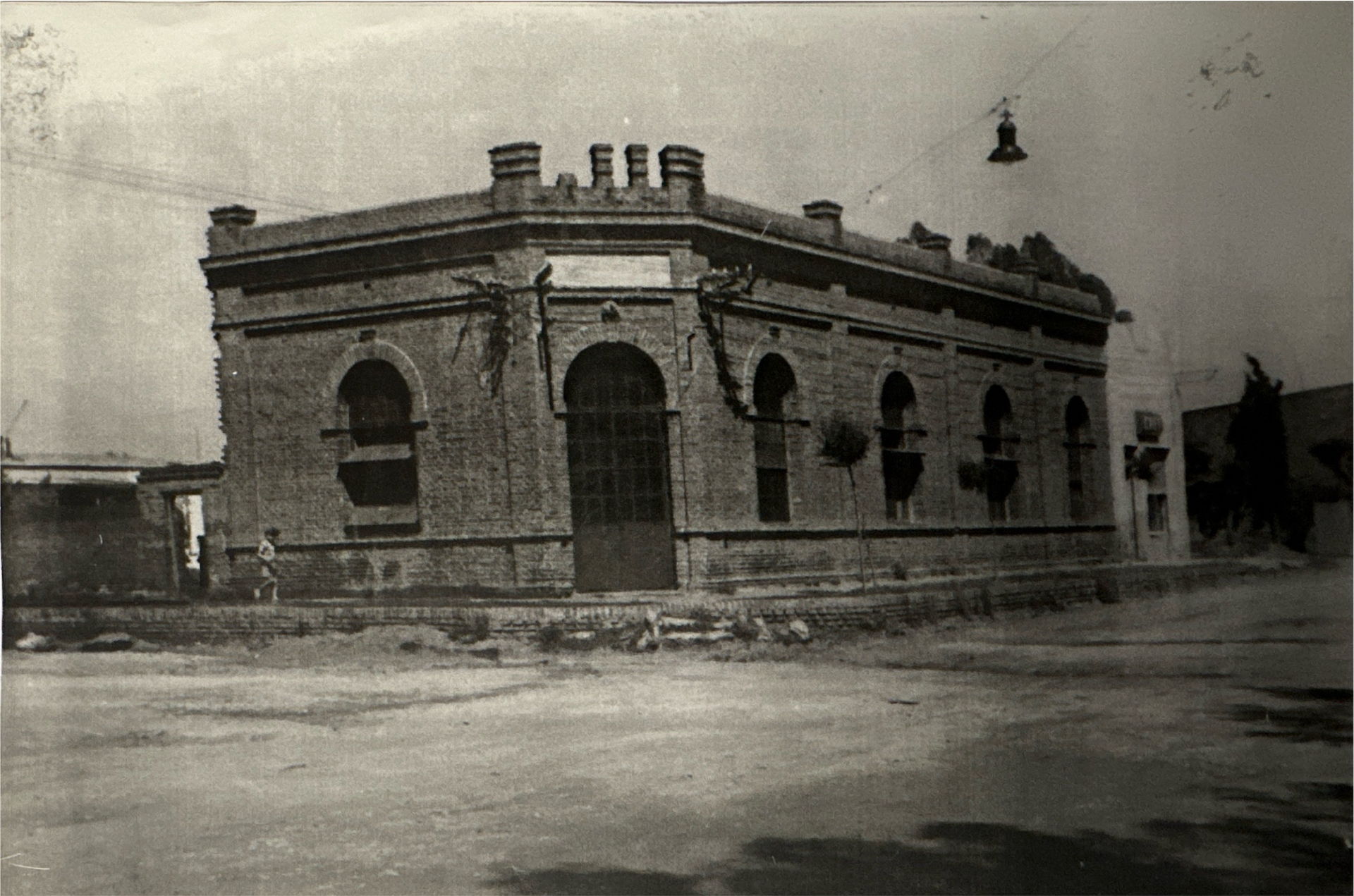 Edificio de ladrillo con ventanas y puerta arqueadas en una esquina. Se ve una persona cerca.