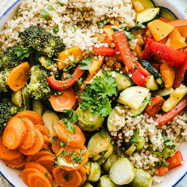 Colorful bowl of quinoa with roasted vegetables: broccoli, carrots, peppers, zucchini, and Brussels sprouts.