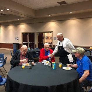 A group of men are sitting at a round table eating food.