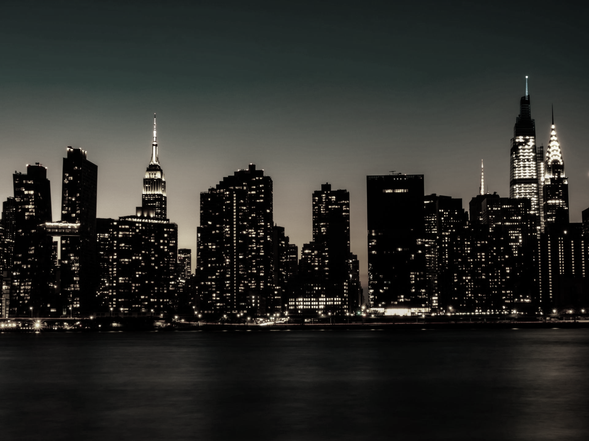 New York City skyline at night with lights reflecting on the water.