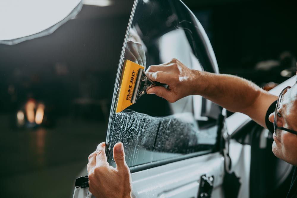 A man is applying tinted glass to a car window.