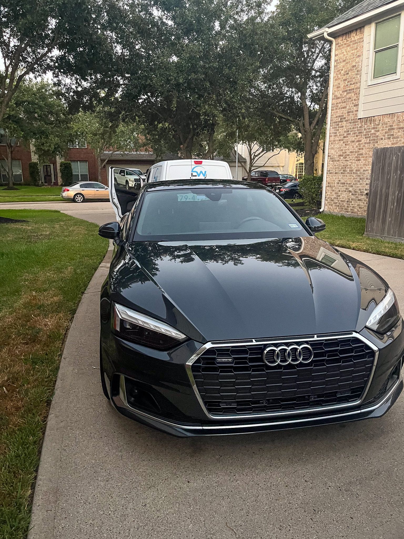 Black Audi sedan parked on a residential driveway beside an apartment building and trees.