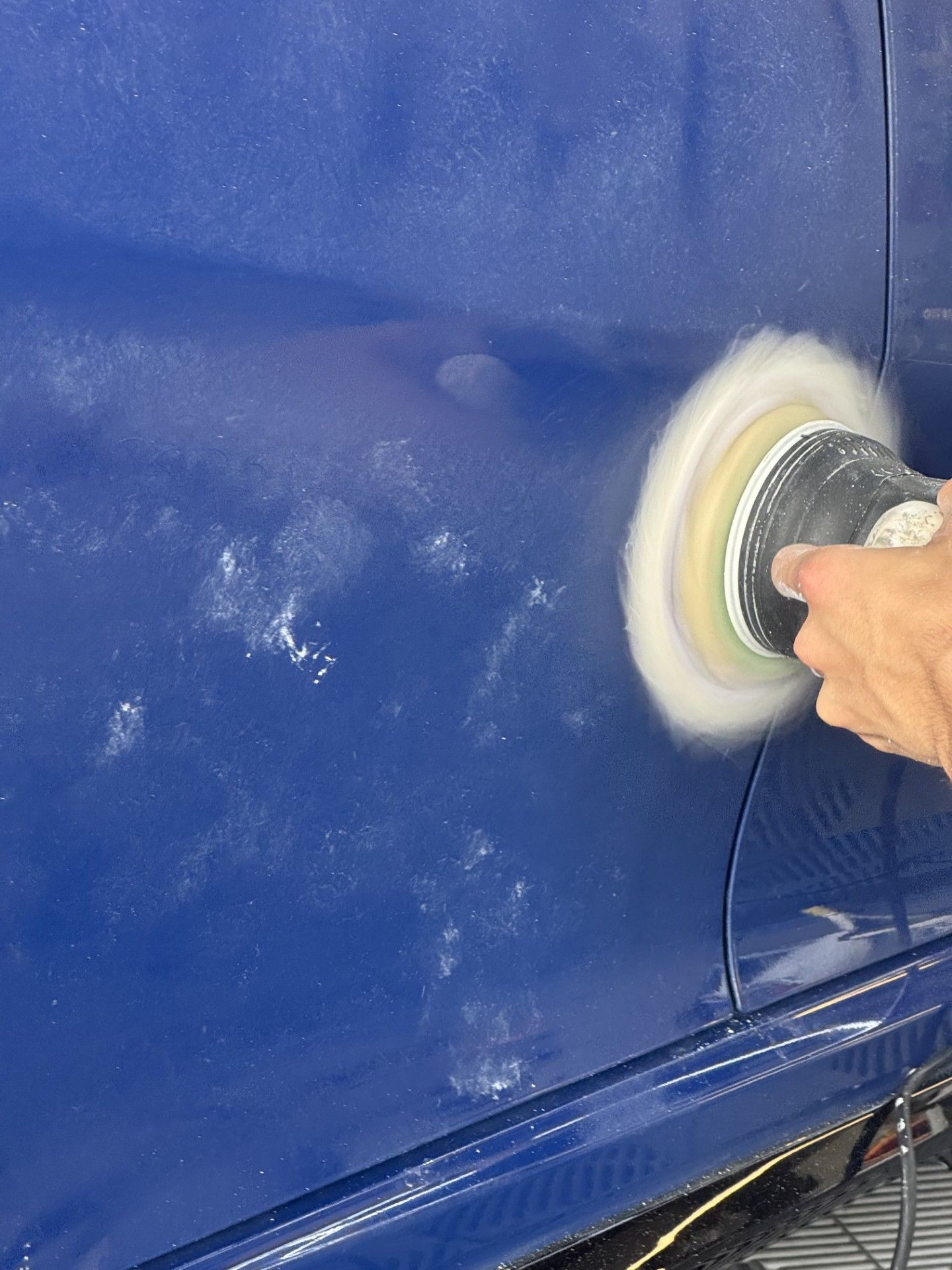 A person wearing black gloves is polishing the hood of a red car.