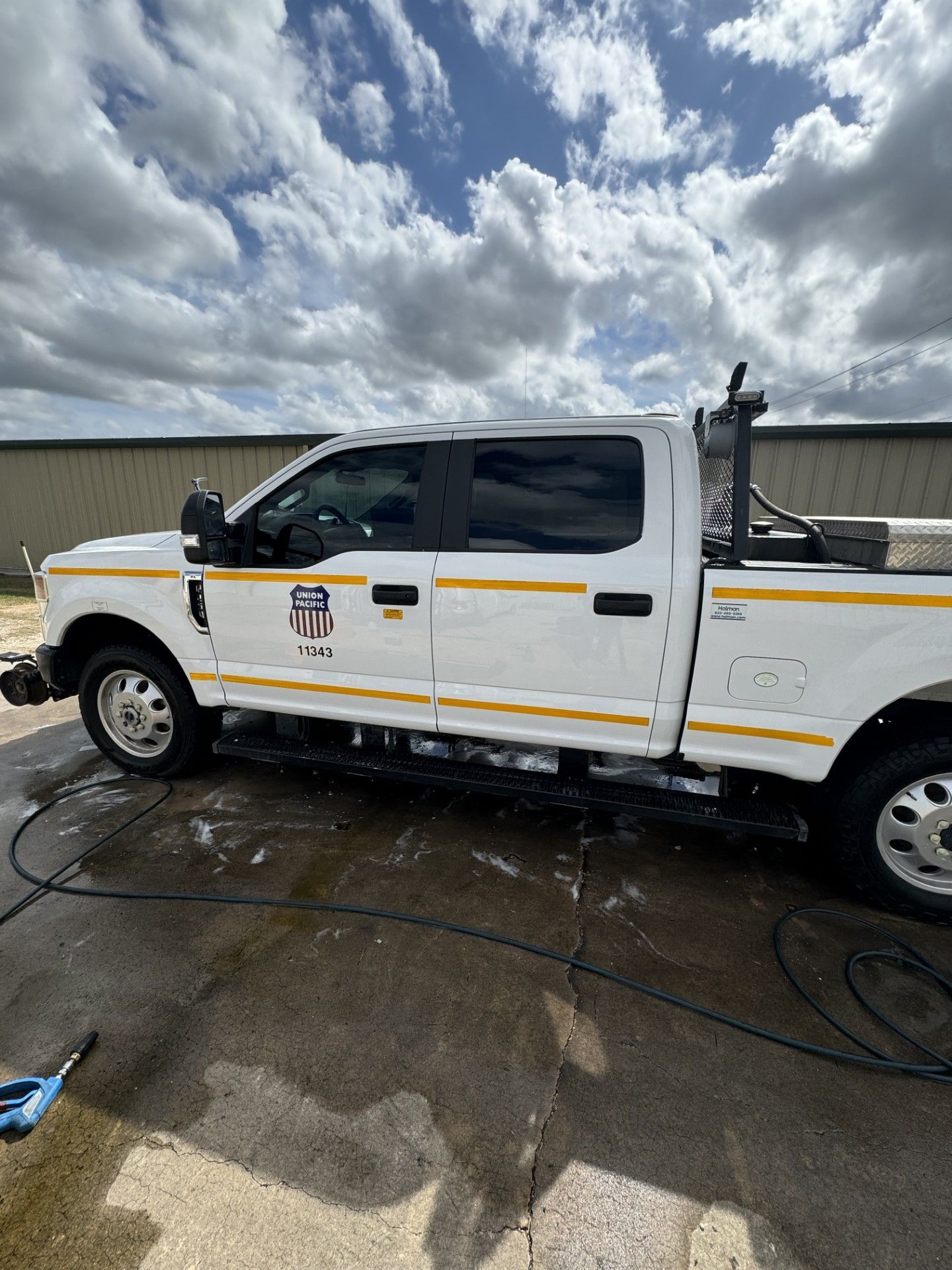 White utility pickup truck with yellow stripes parked on a wet lot under cloudy skies