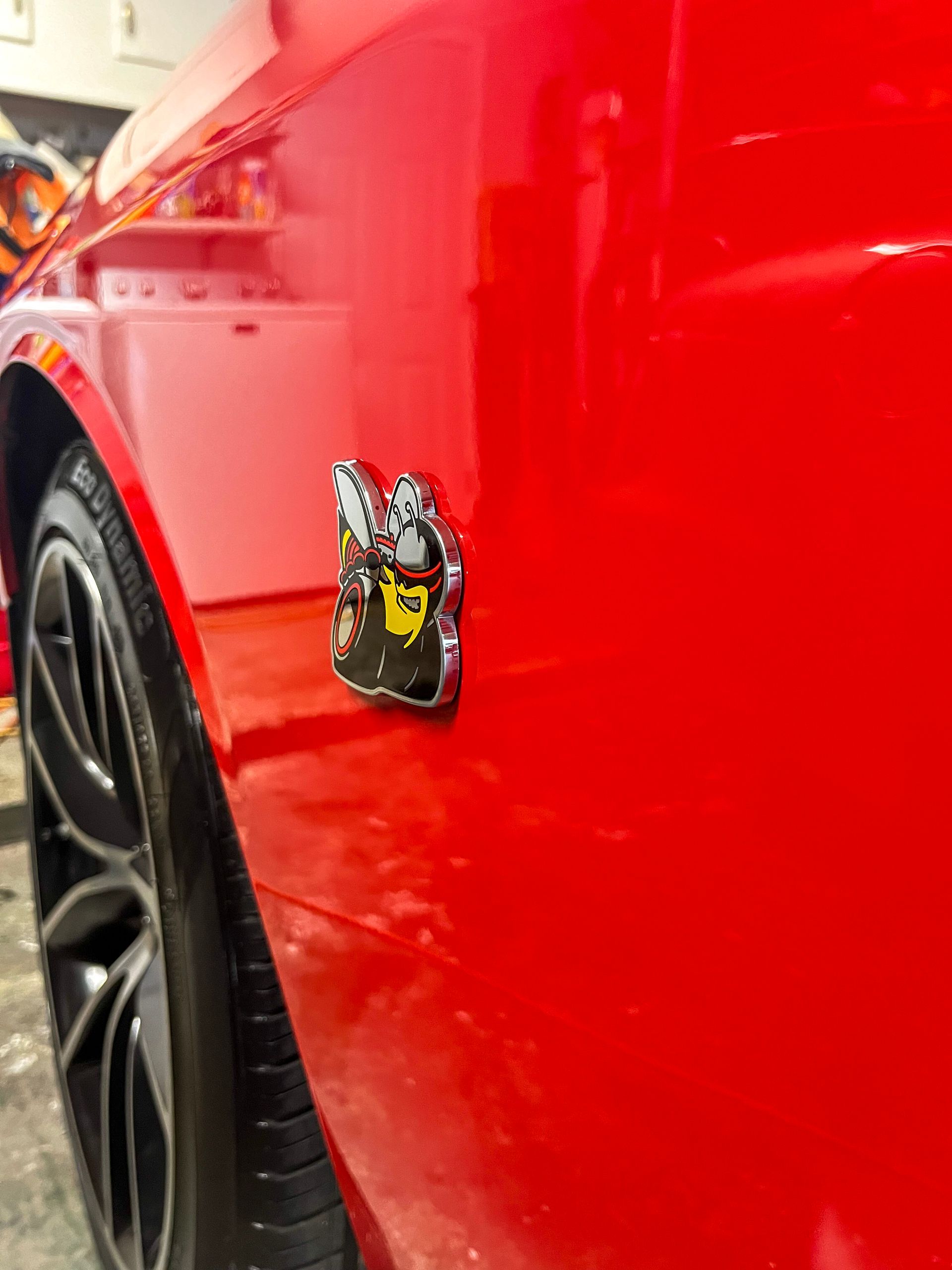 Red car close-up with a small racing badge on the side panel and wheel visible