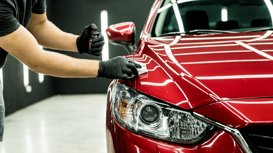 Detailing worker polishing a red car’s front fender with black gloves in a garage