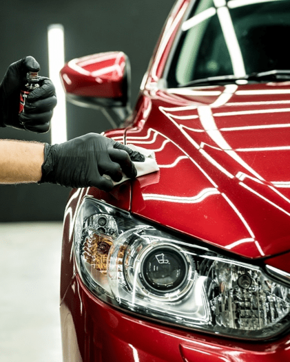 A person wearing black gloves is polishing the hood of a red car.