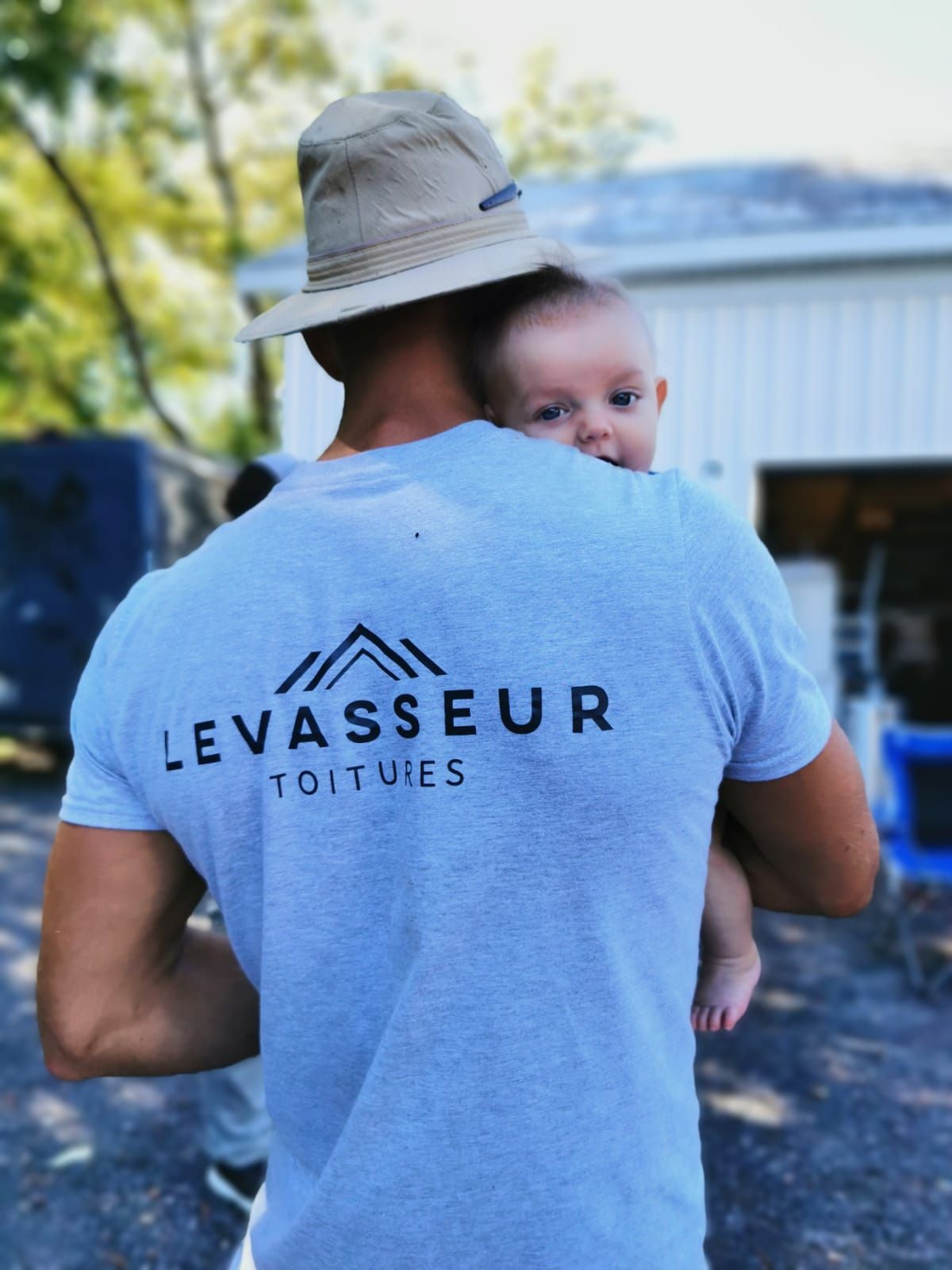 Un homme portant un t-shirt Levasseur tient un bébé