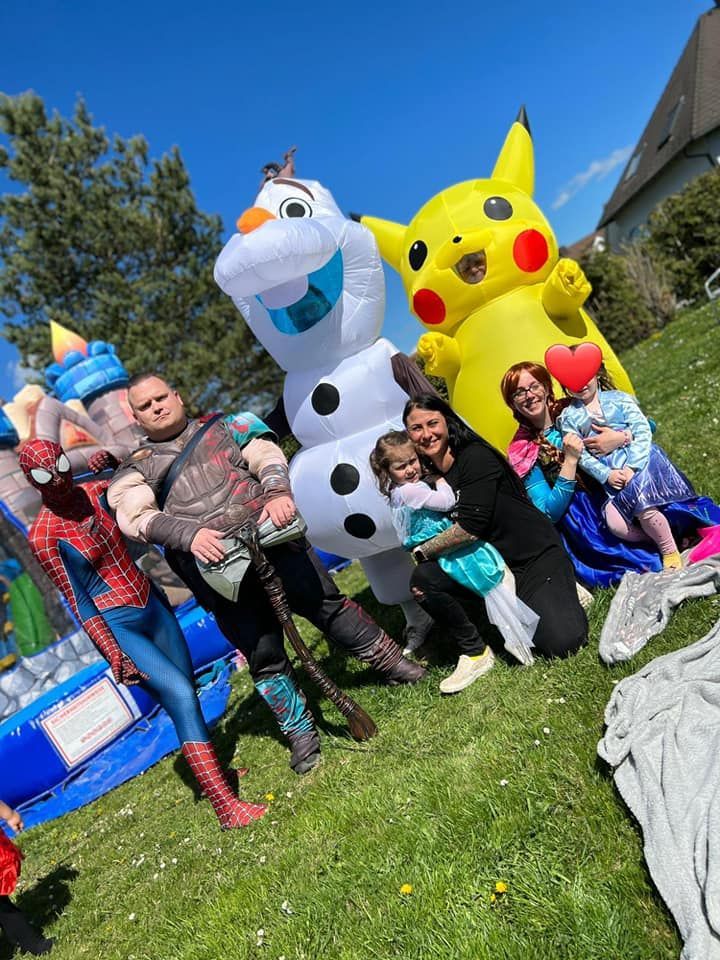 Eine Gruppe von Menschen posiert für ein Foto mit aufblasbaren Figuren wie Olaf und Pikacchu mit Superhelden.