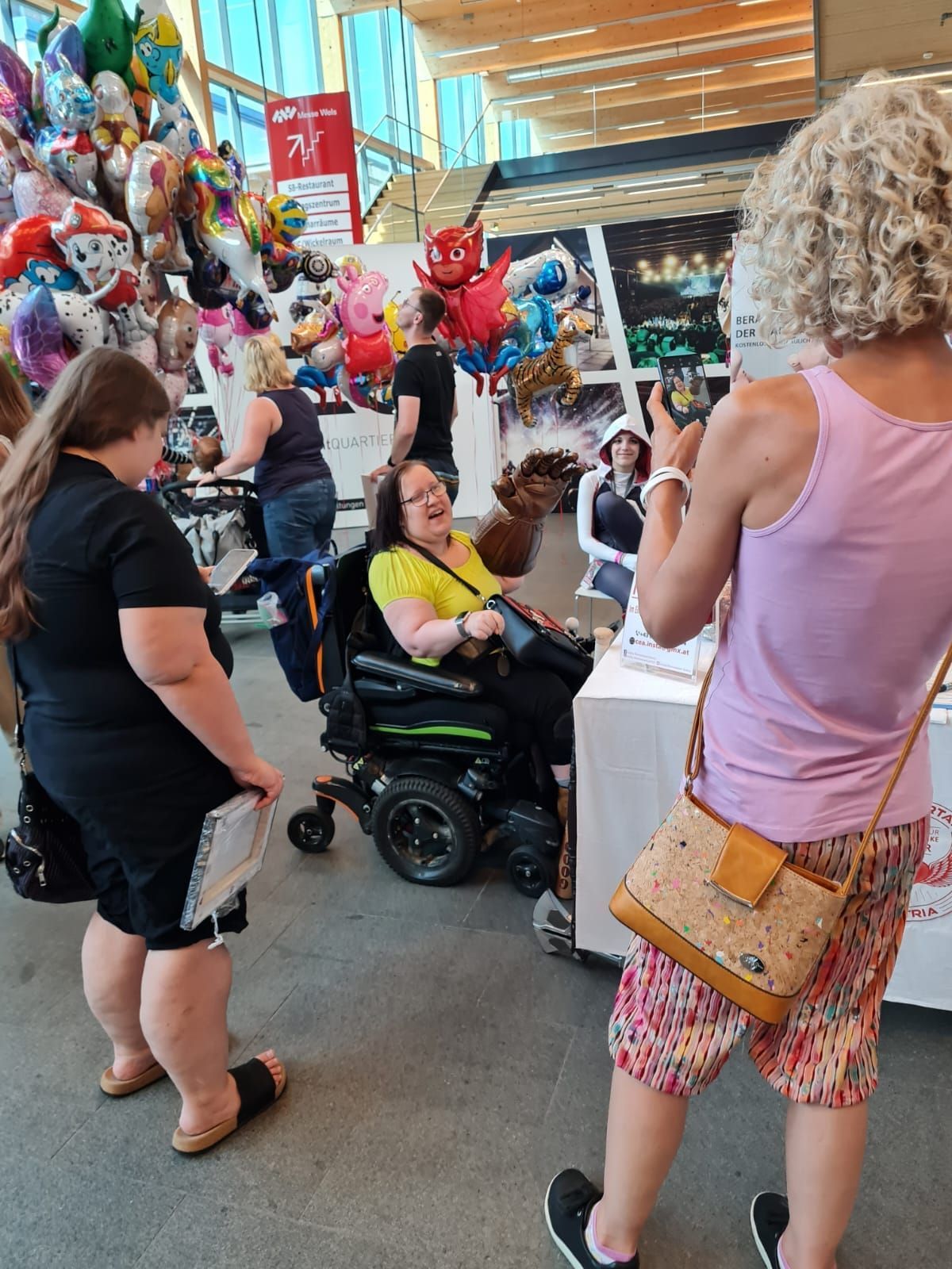 Eine Frau im Rollstuhl wird von einer Frau in einem rosa Tanktop fotografiert.