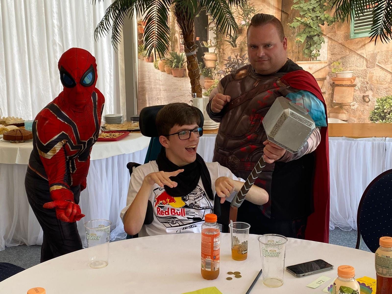 Ein Mann in einem Spiderman-Kostüm steht neben einem Jungen im Rollstuhl.