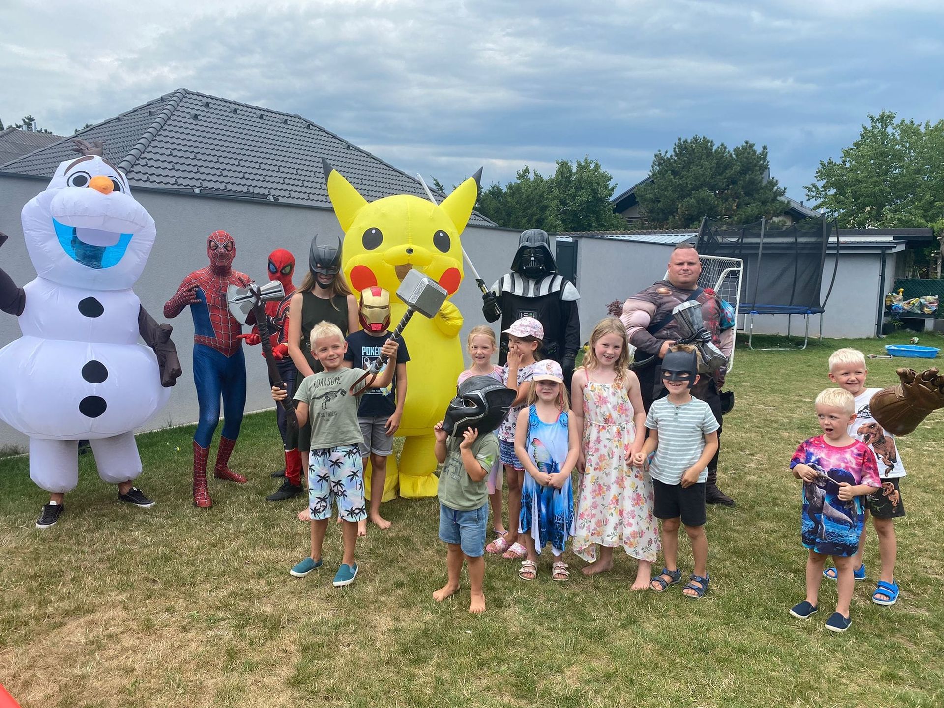 Eine Gruppe Kinder posiert mit verleideten Superheldn und aufblasbaren Figuren Olaf und Pikatchu für ein Foto.