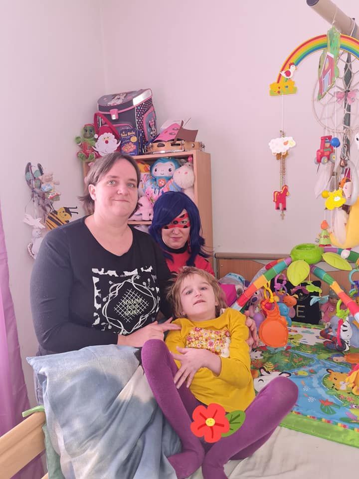 Eine Frau sitzt auf einem Bett und hält ein kleines Mädchen mit kostümierter Frau als Ladybug.