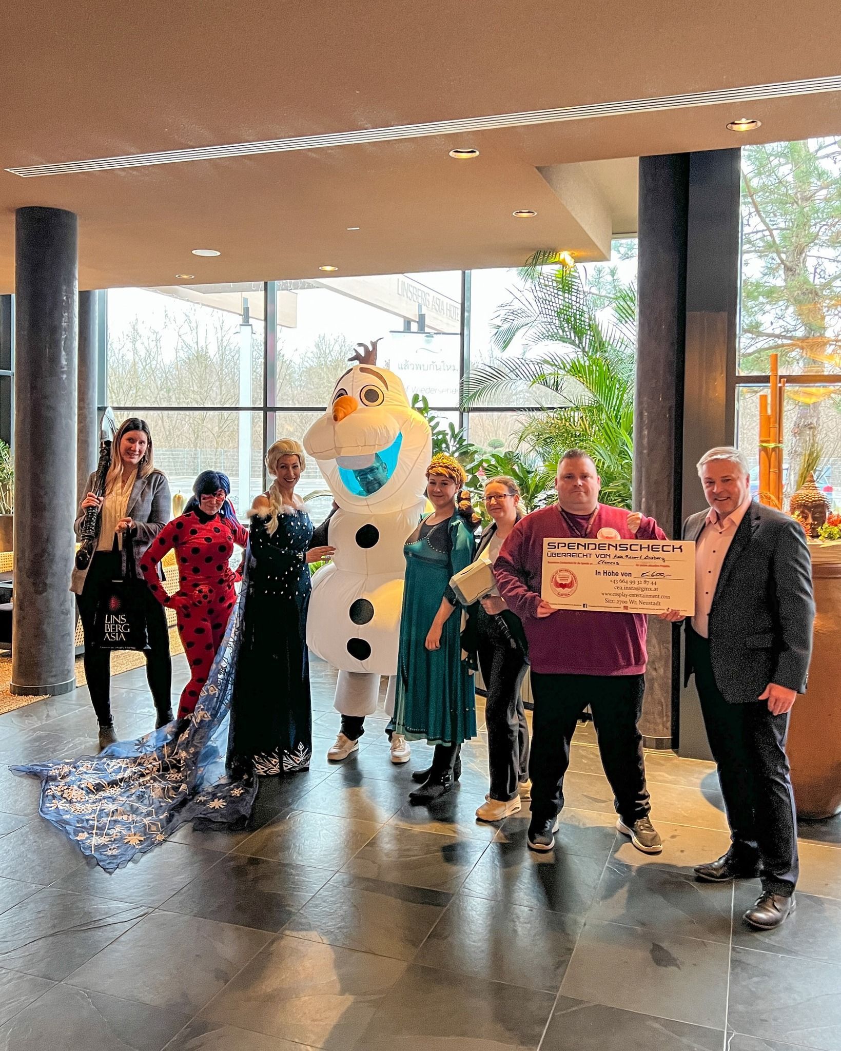 Eine Gruppe von Menschen steht nebeneinander vor einem großen Schneemann Olaf bei einer Spendenübergabe.