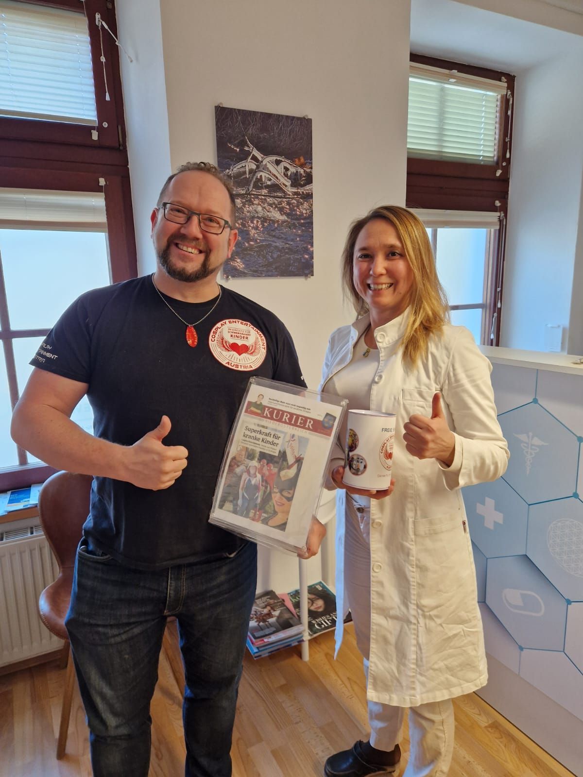 zwei Personen von Cosplay mit Presseartikel von Kurier eingeramt und Spendendose