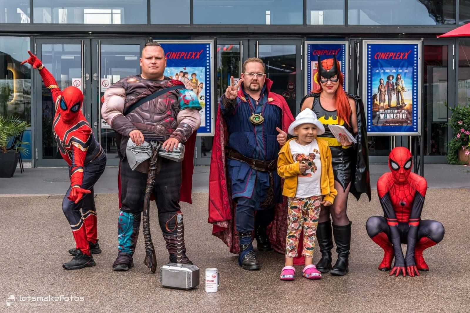 Eine Gruppe von Menschen in Superheldenkostümen posiert vor einem Gebäude für ein Foto.
