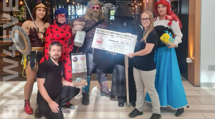 Eine Gruppe kostümierter Menschen posiert für ein Foto bei einer Spendenscheckübergabe.