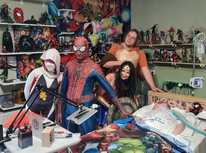 Eine Gruppe von Menschen in Superheldenkostümen steht um ein Krankenbett eines Schützlings herum.