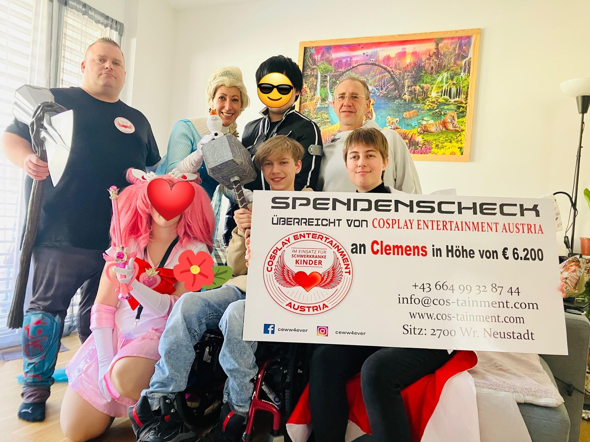 Eine Gruppe von Menschen in Superheldenkostümen hält in einem Wohnzimmer einen Scheck in der Hand.