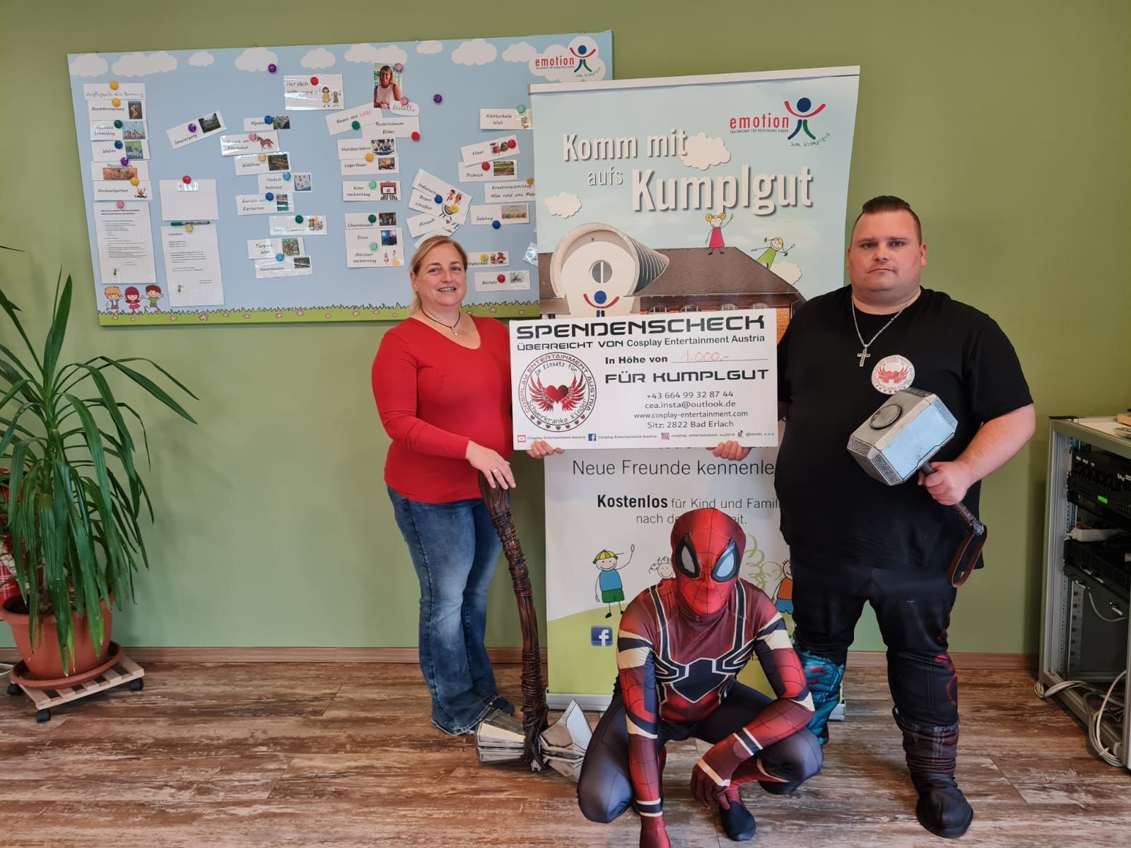 Eine Gruppe von Menschen in Superheldenkostümen hält in einem Wohnzimmer einen Scheck in der Hand.