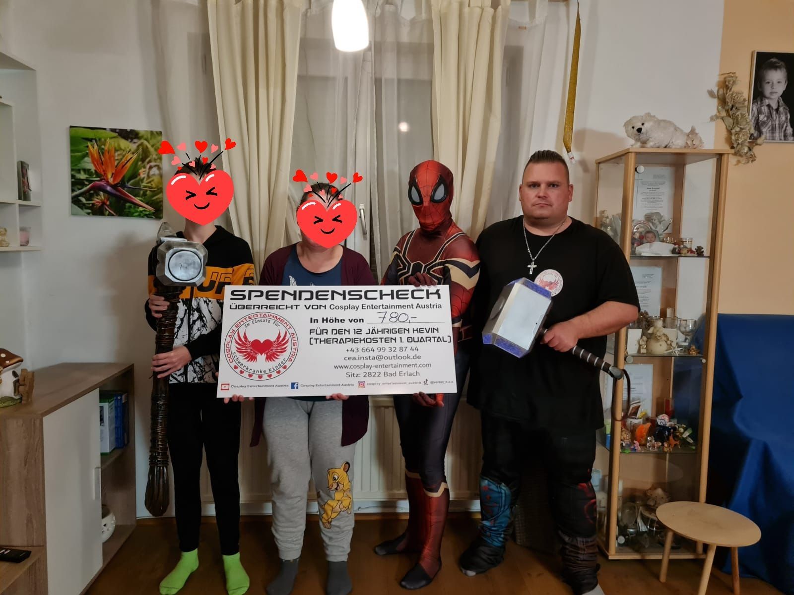 Eine Gruppe von Menschen in Superheldenkostümen hält in einem Wohnzimmer einen Scheck in der Hand.