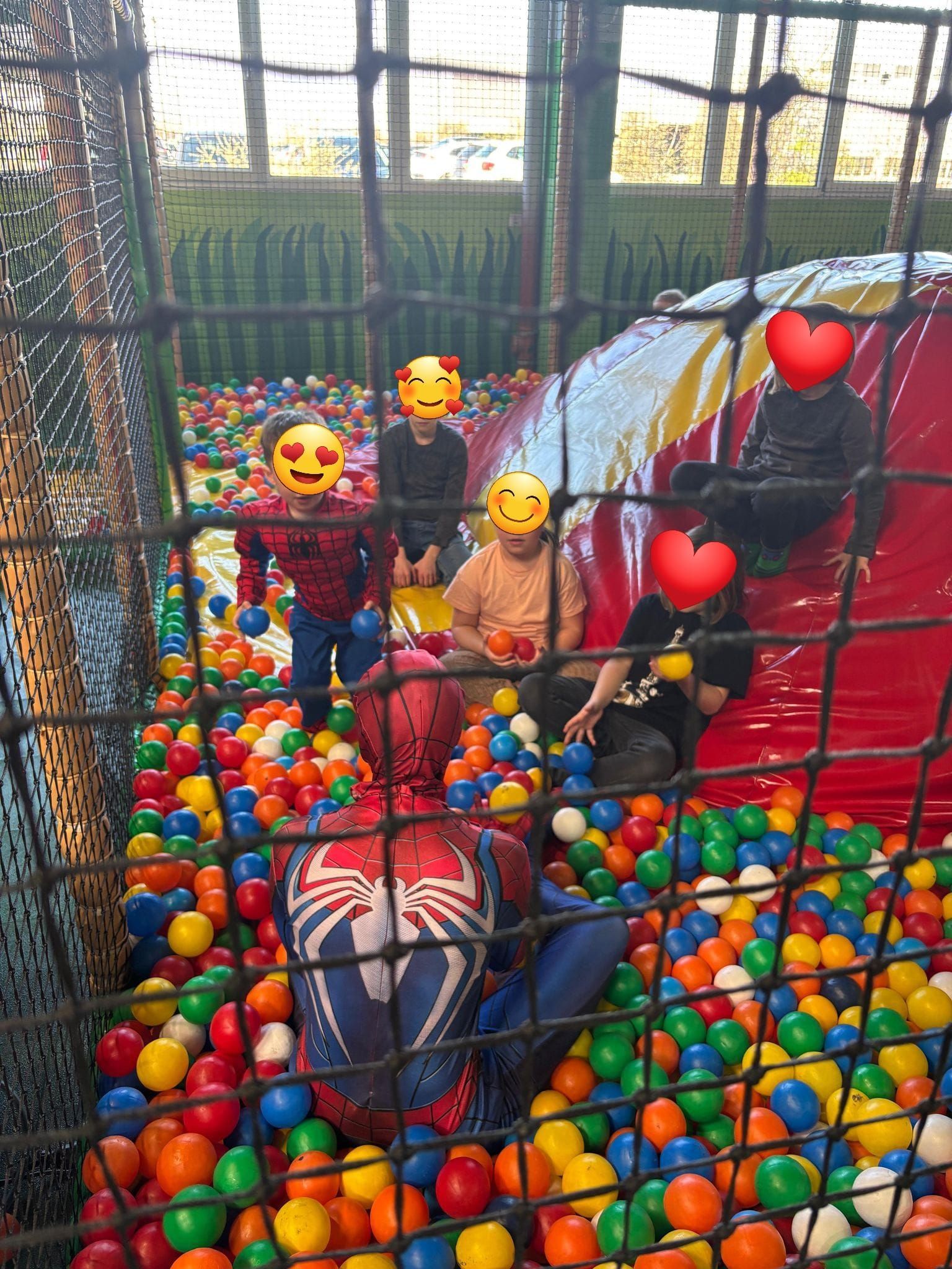 Eine Gruppe Kinder spielt in einem Bällebad mit einem als Spiderman verkleideten Mann.