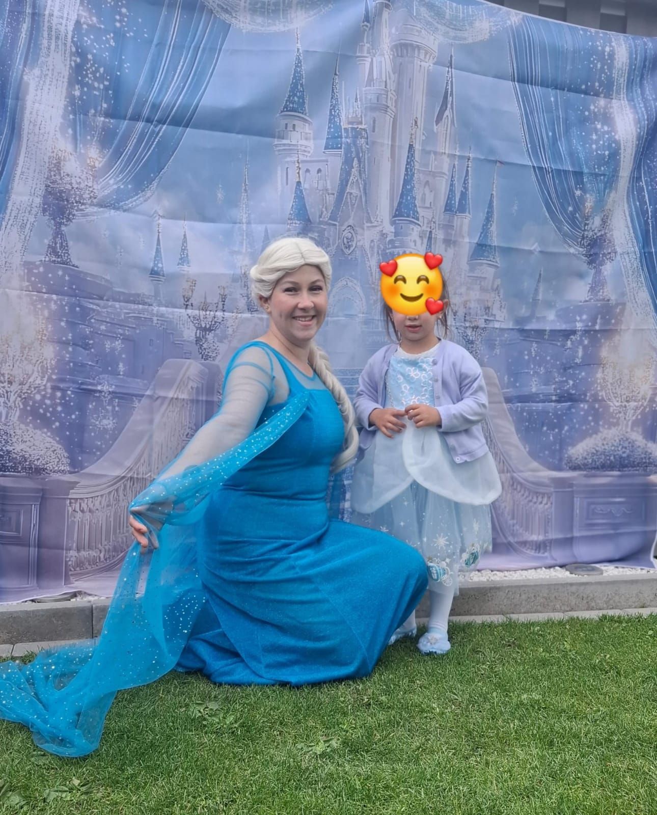 Eine als Elsa verkleidete Frau kniet neben einem kleinen Mädchen vor einem Schloss.