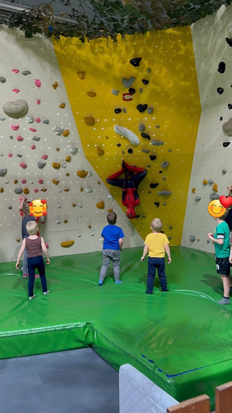 Eine Gruppe Kinder steht vor einer Kletterwand an der ein kostmümierte Person als Spiderman sitzt.