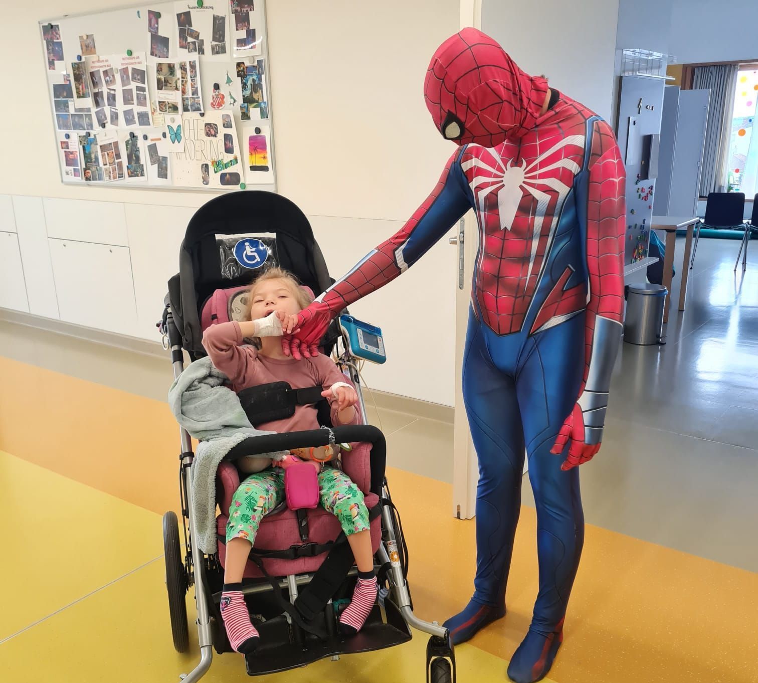 Ein Mann in einem Spiderman-Kostüm schiebt ein kleines Mädchen im Rollstuhl