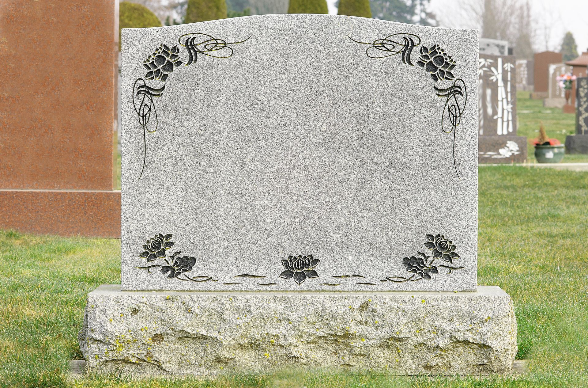 Grey tombstone with flowers in a cemetery featuring custom granite grave headstone in Pittsford, NY 