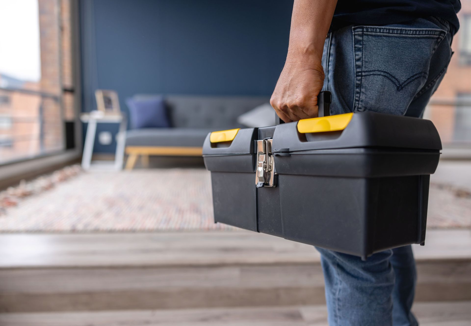 Person holding a black toolbox with yellow latches in a living room.