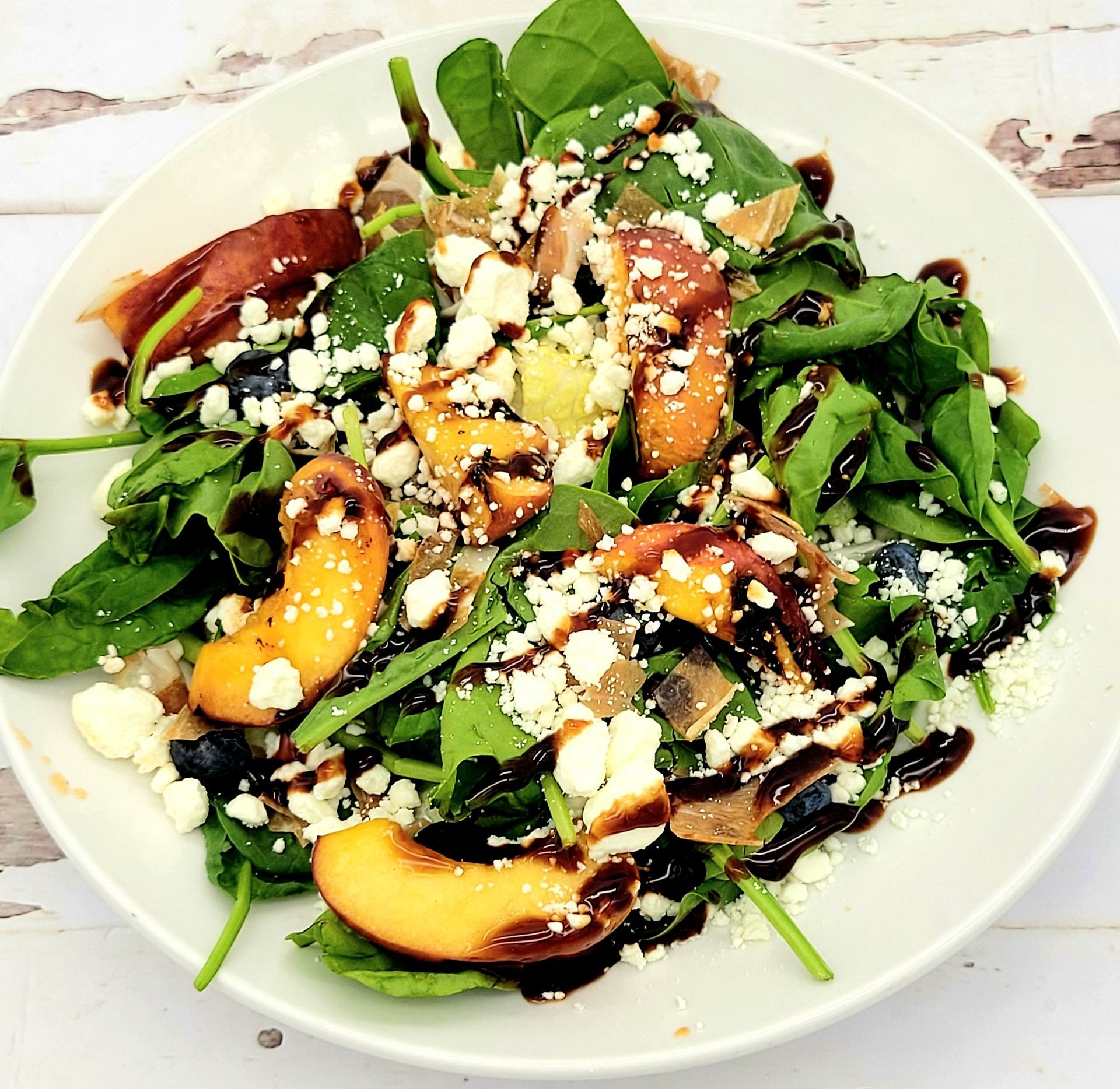 A salad with peaches and spinach on a white plate