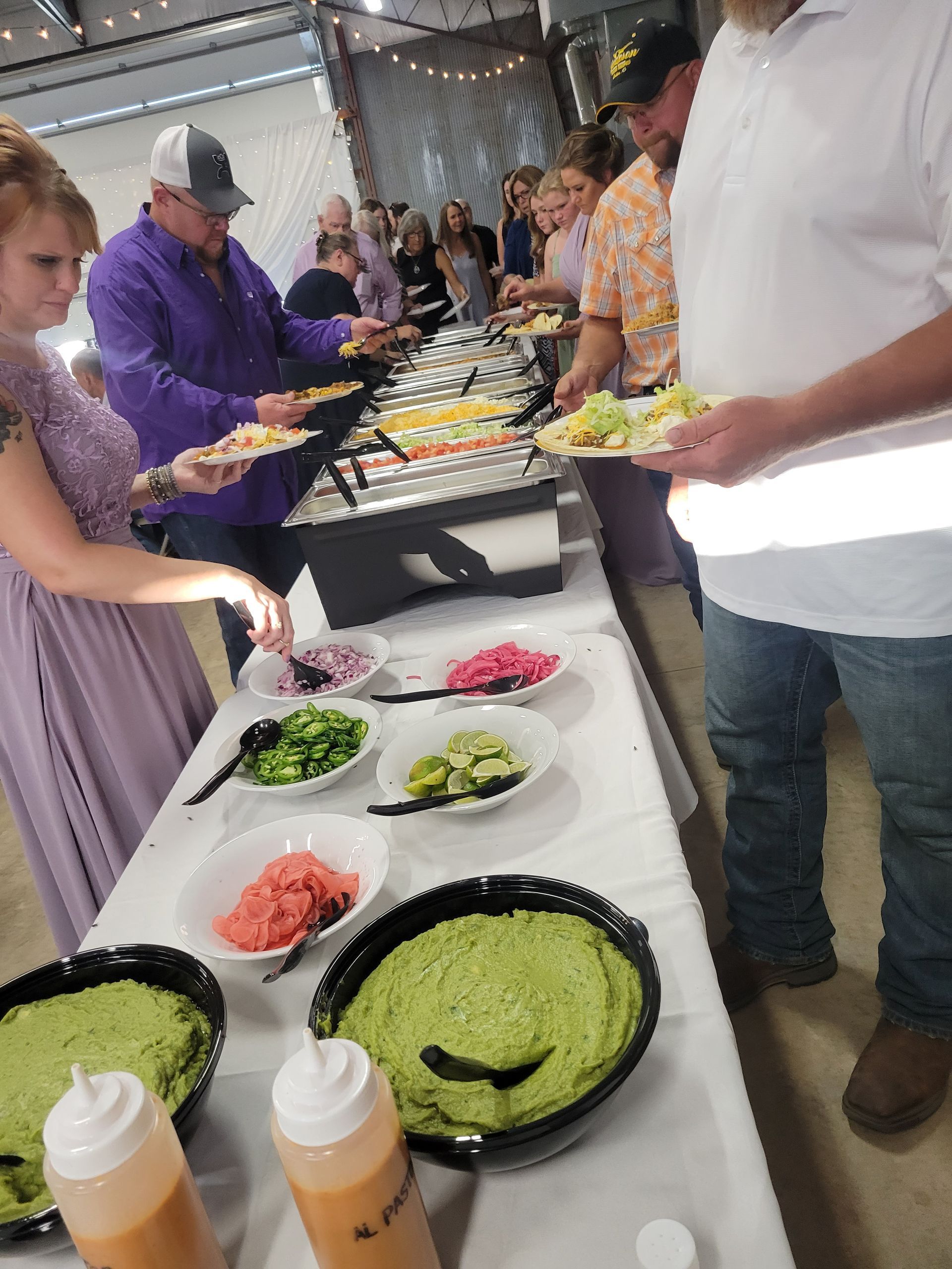 A group of people are standing around a table filled with catered food.