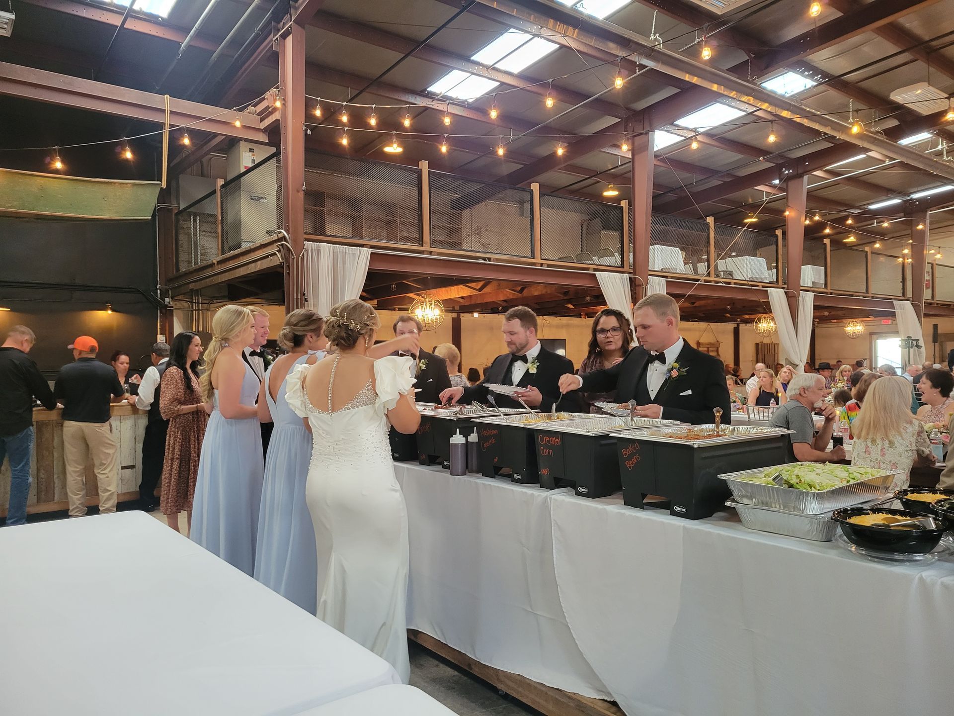 A group of people are standing around a buffet line at a wedding reception.