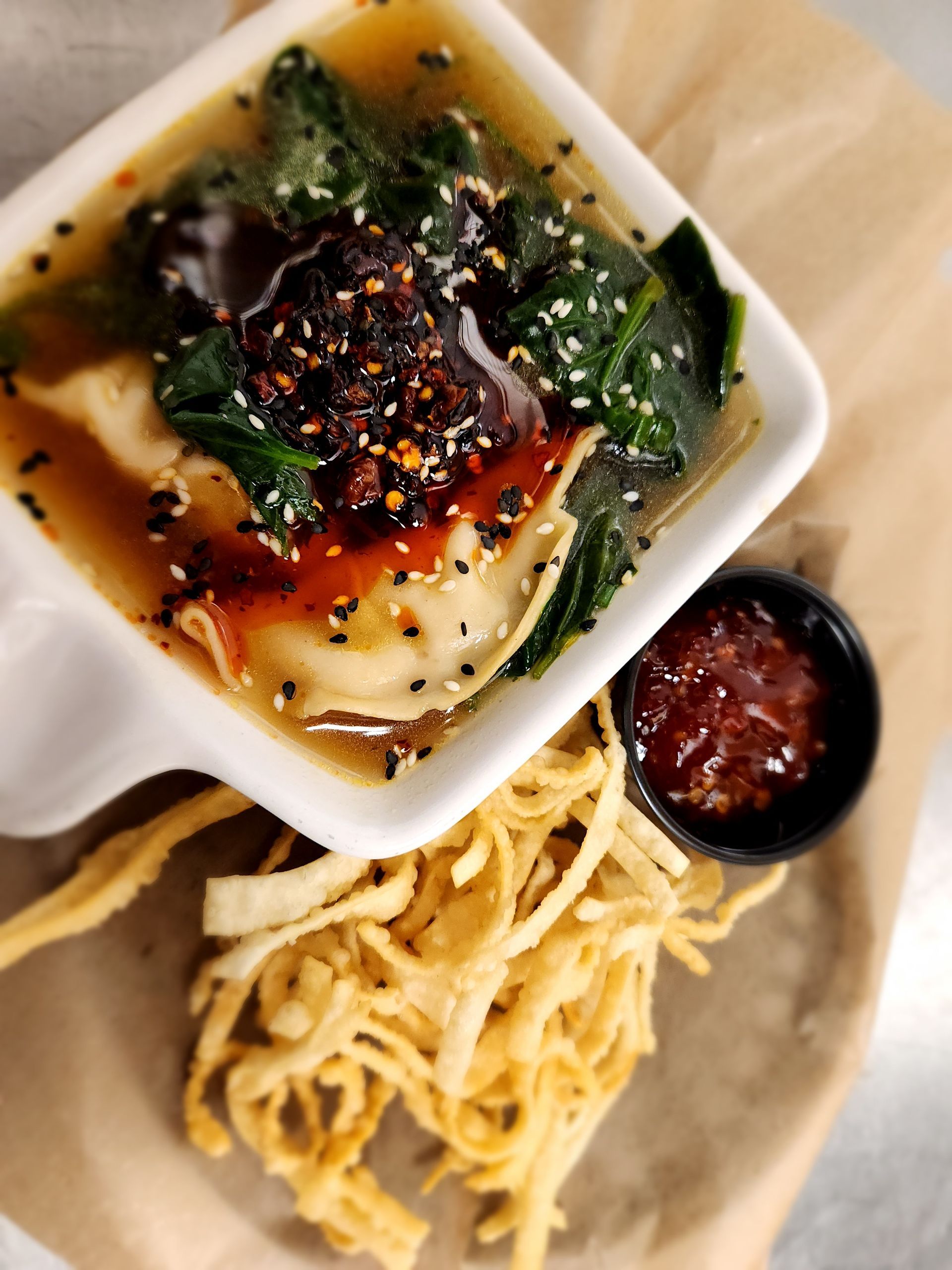 A bowl of soup with noodles and sauce on a table.