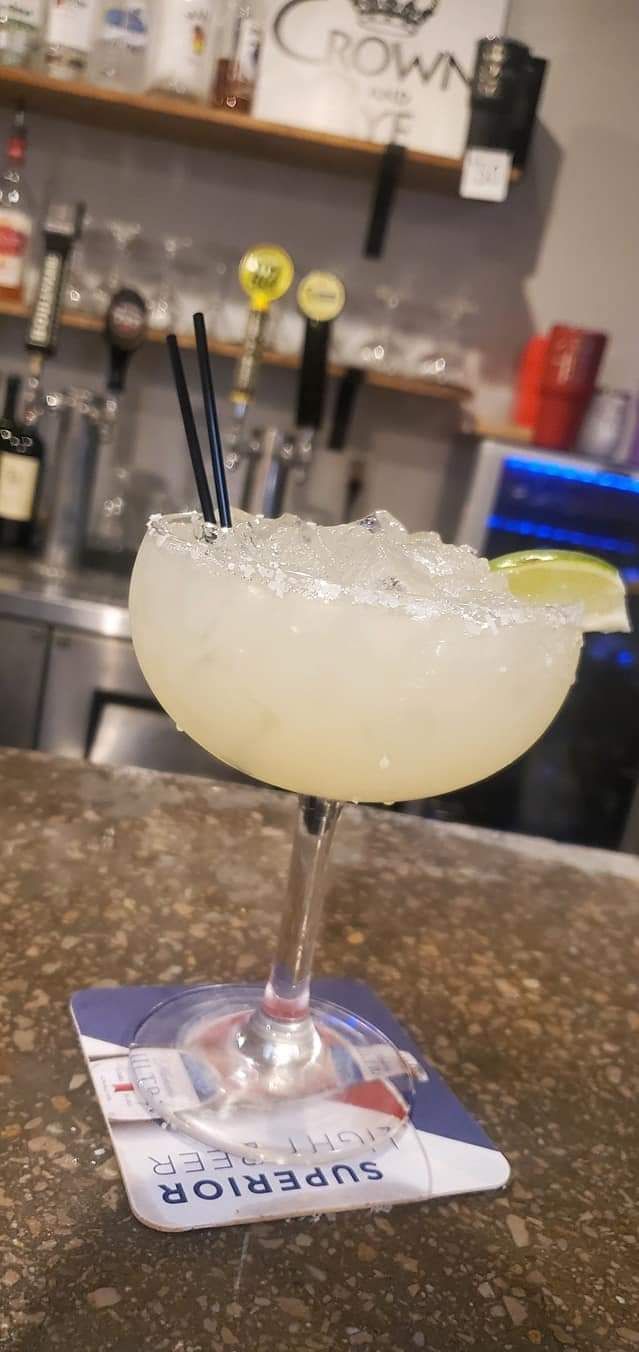 A margarita is sitting on a coaster on a bar.