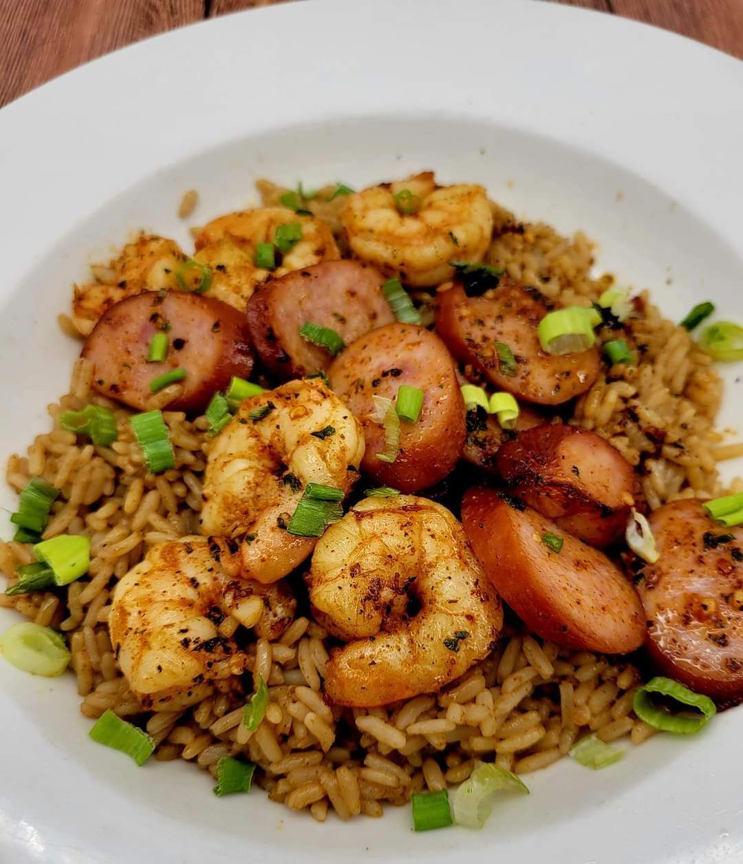 A white plate topped with shrimp and sausage on rice.