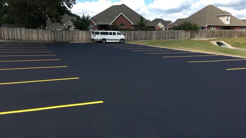 Empty parking lot with yellow lines, a white van, and houses in the background.