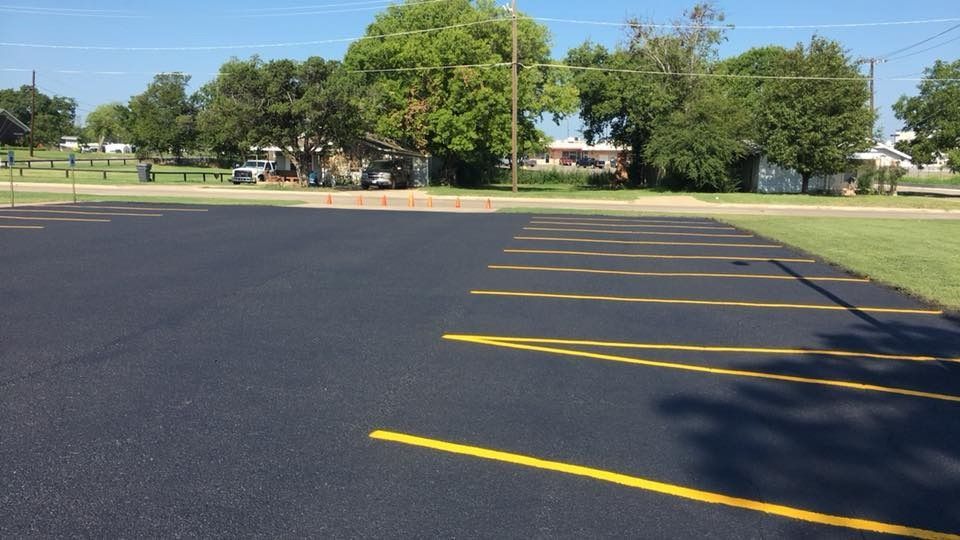 Empty parking lot with yellow painted lines beside trees and a grassy park area