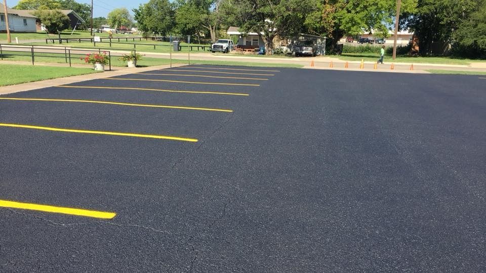 Empty paved parking lot with yellow lines beside a grassy park and trees